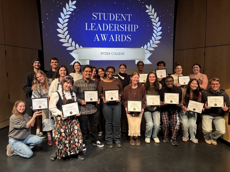 Group photo of student award winners on Benson stage underneath a blue awards banner