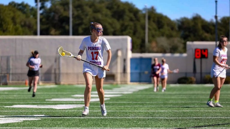 Sydney Landauer runs across the field with a yellow ball in the net of her lacrosse stick.