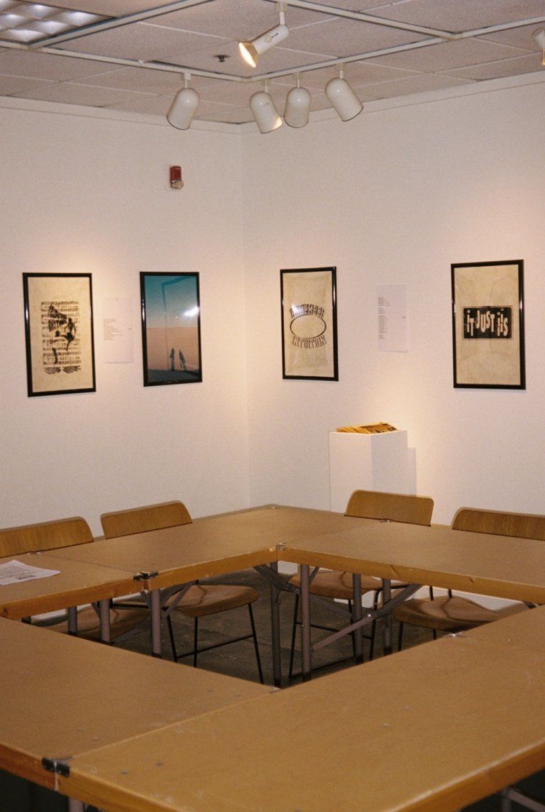 Four prints of texts and photos hang on the walls and four tables are arranged in a square.