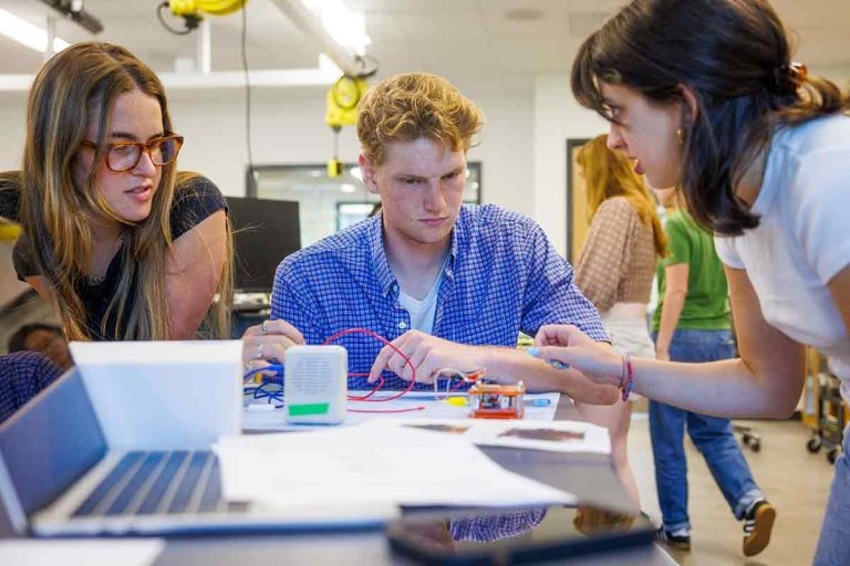 three students work on a project together in a physics lab