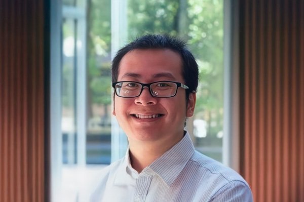 Average Phan has close-cropped black hair and wears glasses and a white collared shirt while standing in an office.