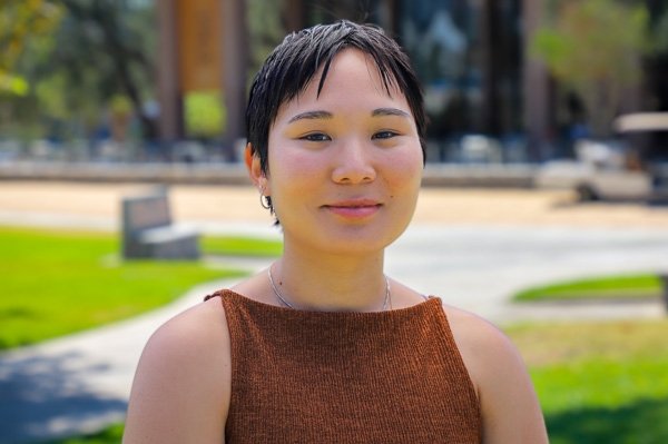 Maria Paz Almenara has close-cropped straight black hair and wears a sleeveless copper top while standing outdoors.
