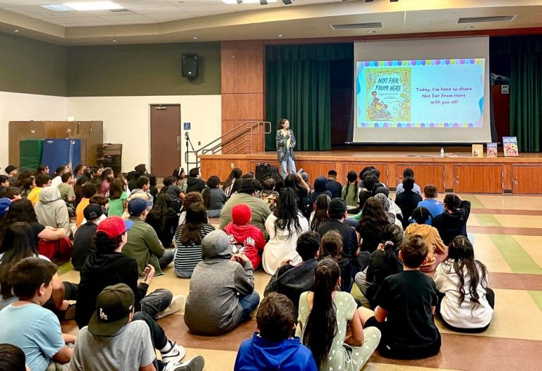 Nydia Armendia-Sanchez shows a slideshow presentation of her book titled Not Far From Here to an auditorium of elementary school children.