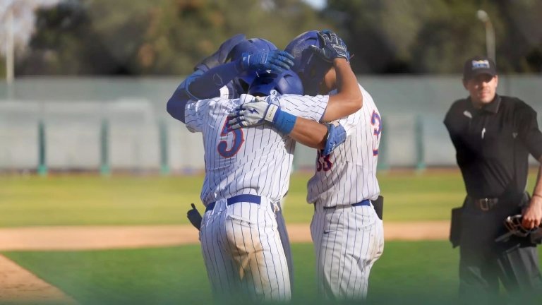 Three members of the Pomona-Pitzer men’s baseball team wearing white and blue uniforms embrace each other on the field.