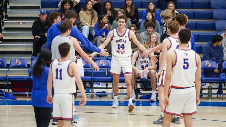 The Pomona-Pitzer men’s basketball team stand in two rows on the court as a team member walks through the middle to give high-fives.