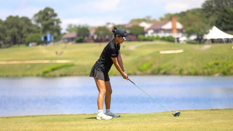 A Pomona-Pitzer women’s golf team member wearing a black uniform prepares to swing a club on the course.