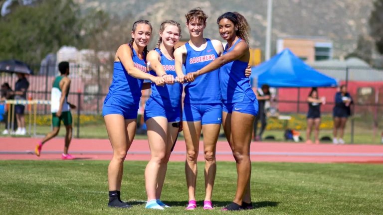 Four members of the Pomona-Pitzer women’s track and field team put their fists together and smile.