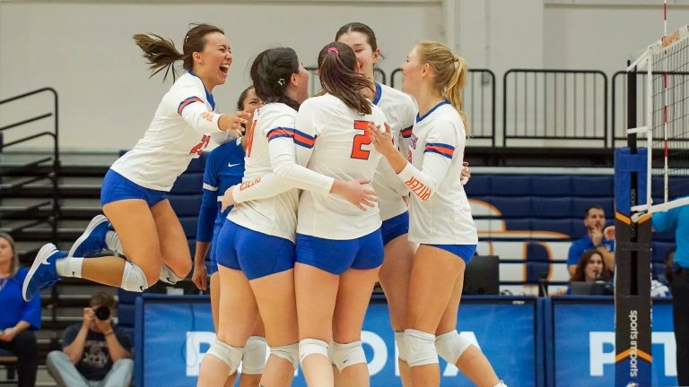 The Pomona-Pitzer women’s volleyball team embrace each other and cheer on the court.