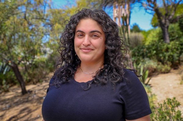 Tahereh Aghdasifar has long curly dark hair and wears a black top while standing outdoors.