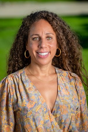 Fely Catan has long curly brown hair and wears hoop earrings and a floral top.