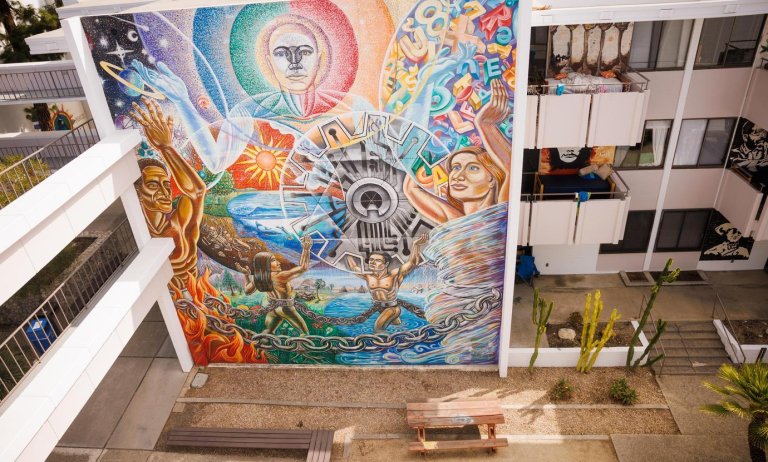 colorful mural with figures of people, celestial shapes, and a being in the center surrounded by concentric beams of color