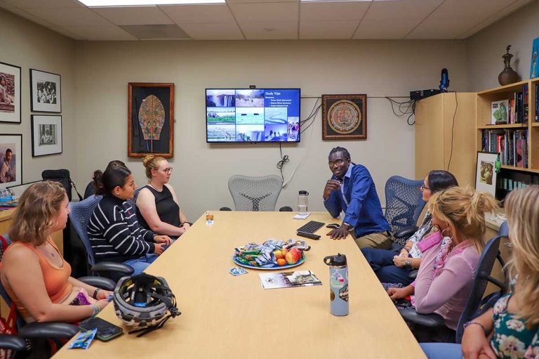 Students sit around a table listening to a presentation
