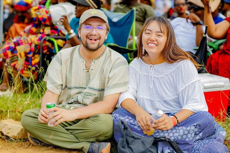 two students sit on the grass at a gathering