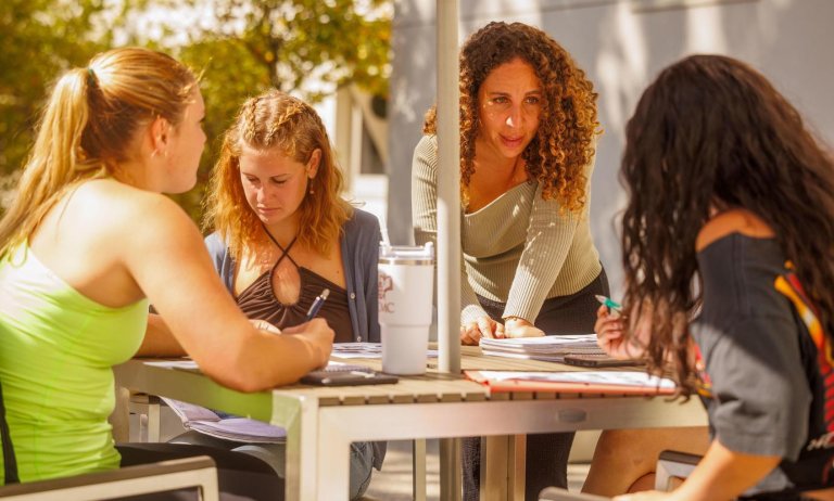 Professor Fely Catan works with students at tables outside