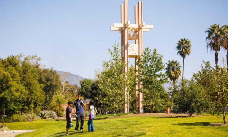 three students talk on the mounds with the clock tower in the background