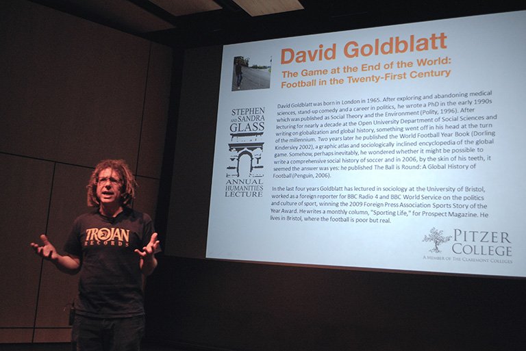 david goldblatt stands on a stage in front of a screen during a lecture