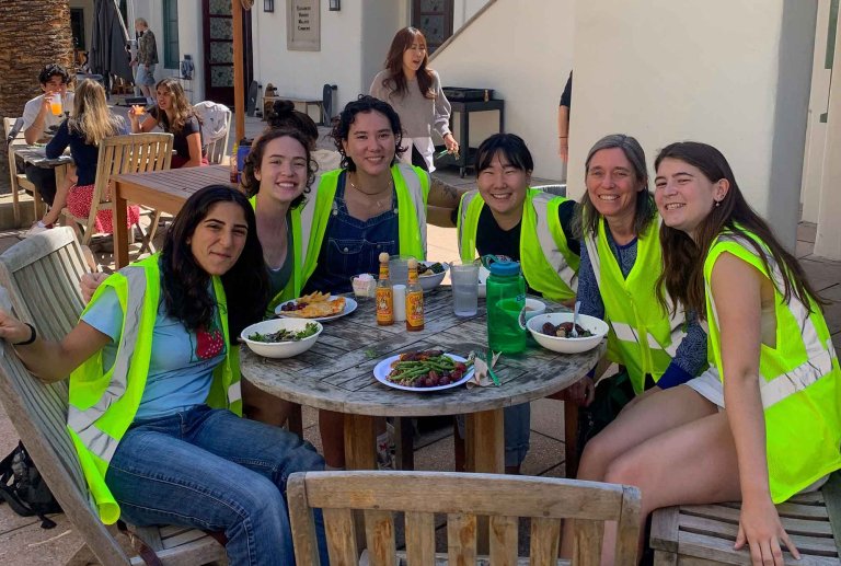 students and a professor sit a table with plates of food in front of them. 