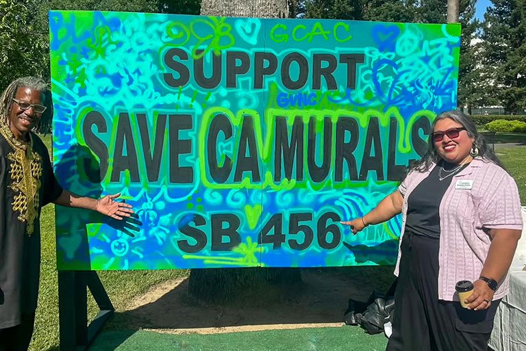 Griselda Suarez and unidentified person pose in front of a sign that says "support  save CA murals SB456"