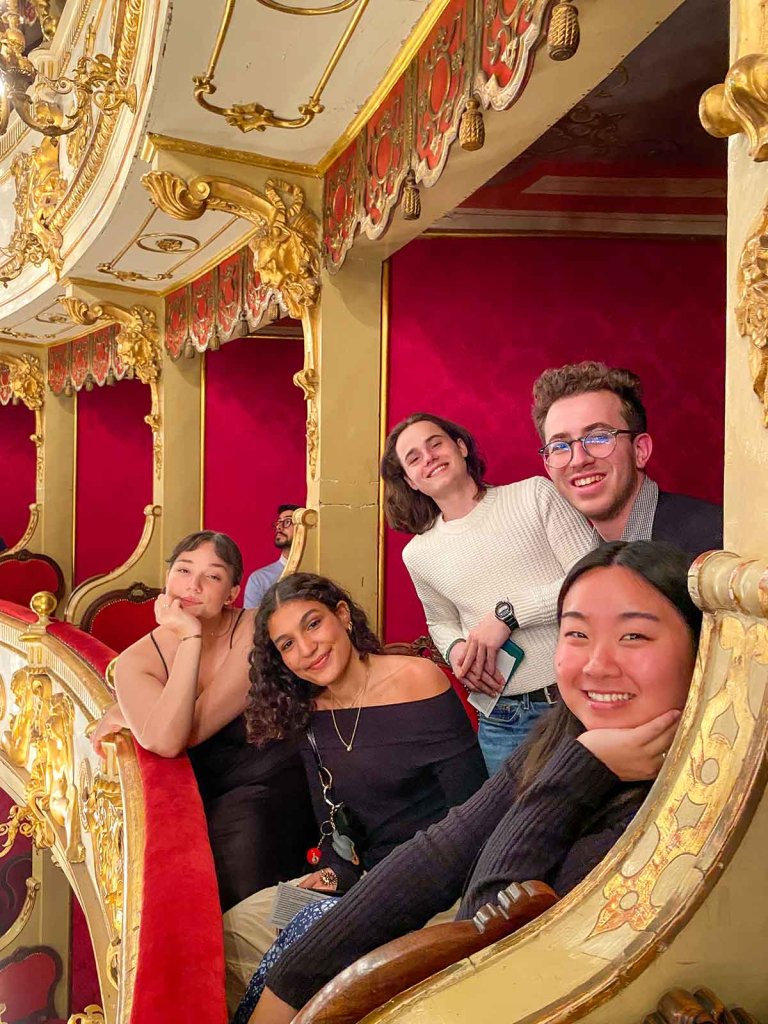 students sit in an ornate opera balcony 