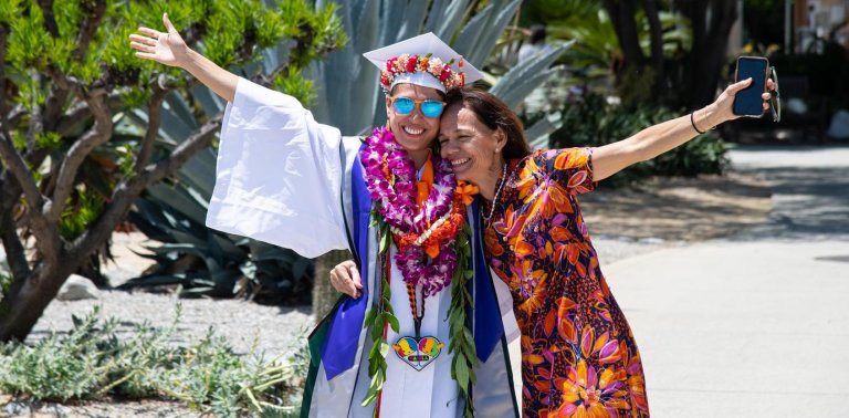 a graduate and family member hug with one arm in the air