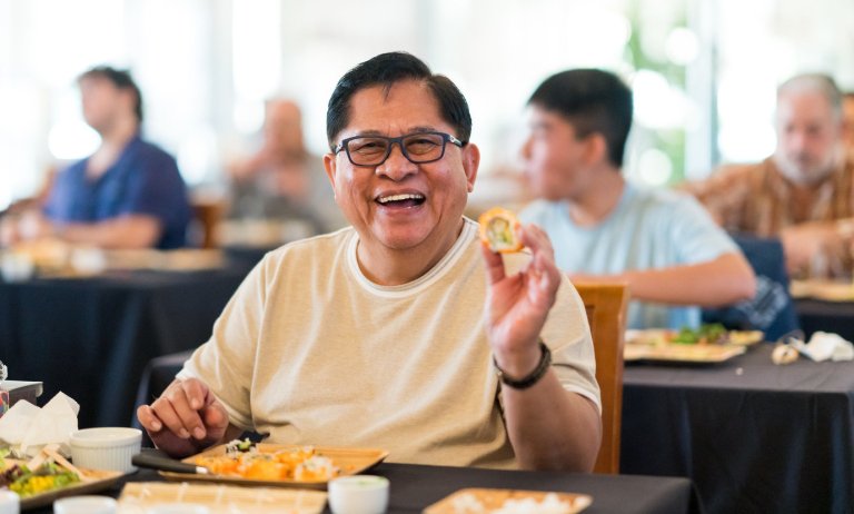 a parents shows off a sushi roll he made during a sushi making workshop