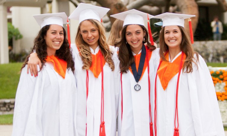 Four students pose on the mounds in their graduation regalia
