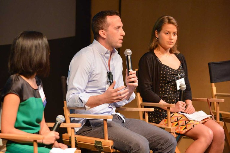 alums sit on a stage in chairs and microphones in their hands