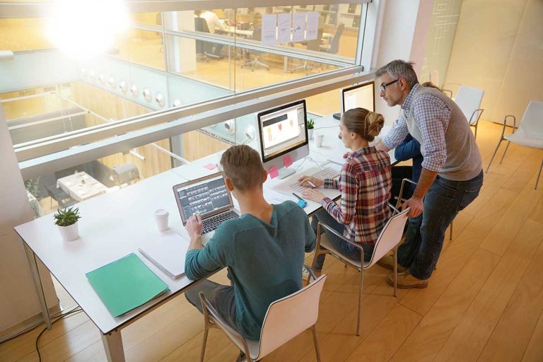 two students sit side by side at computers while a man points to a screen