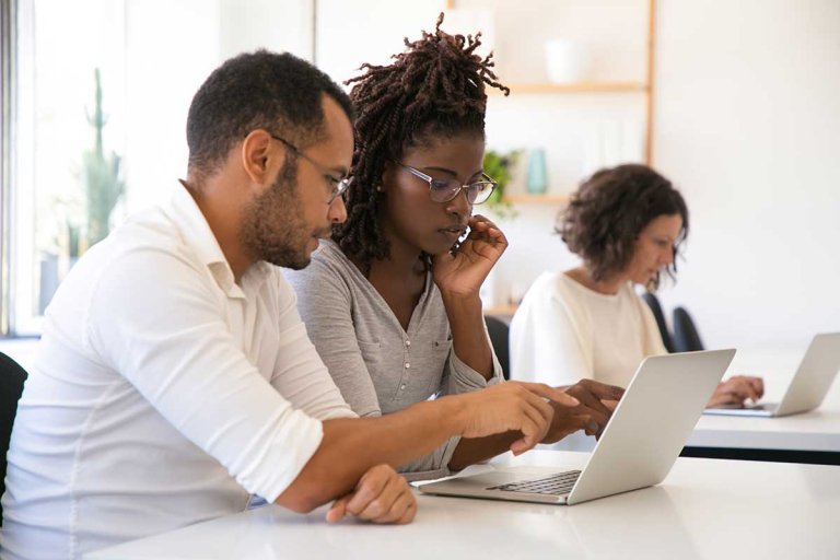 a student sits at a computer with a winter shadowing host in an open office