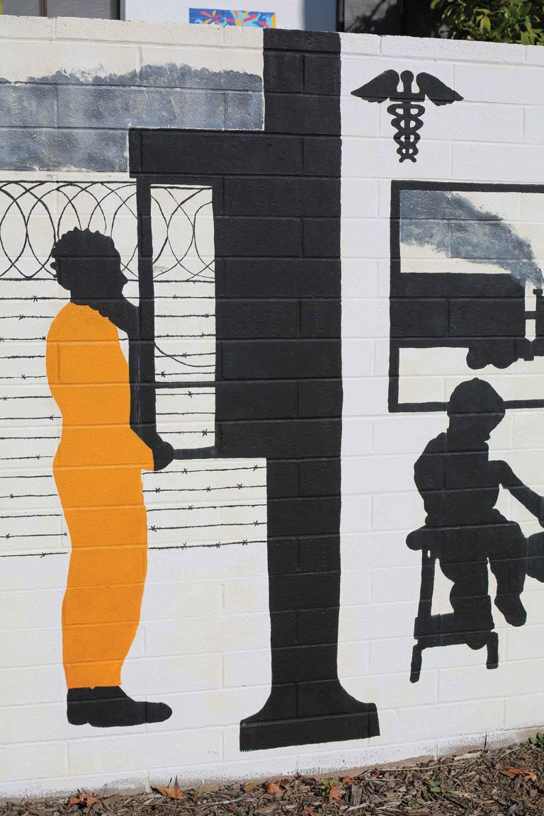 mural of a man in an orange uniform on a payphone and a child on the other side of a wall