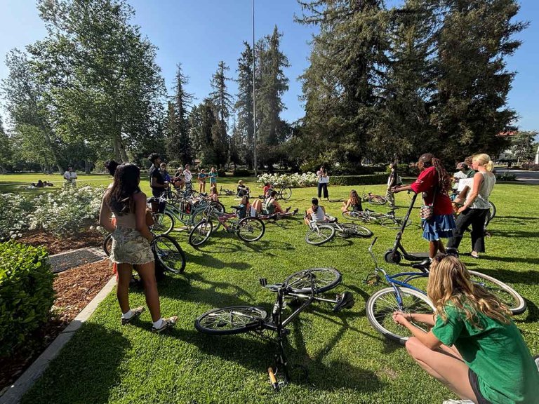 students sit on a lawn with their bikes