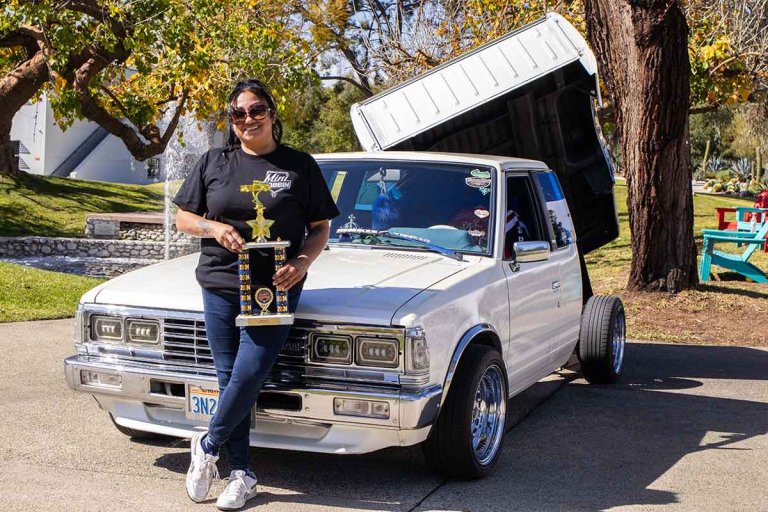a woman stands with a trophy in front of a white lowrider car