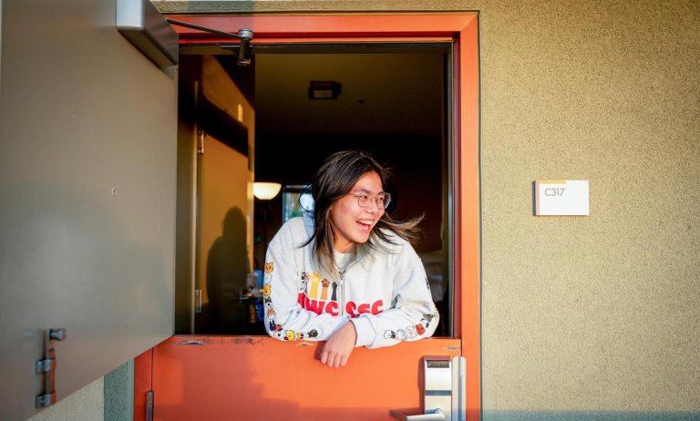 a student looks out of an open orange dutch door of a Pitzer dorm room