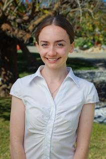 Woman in white blouse smiling. Background is lawn and trees.