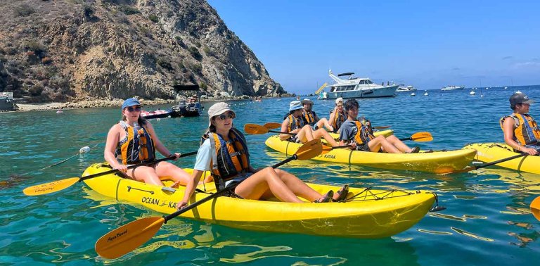 students float in yellow kayaks in the ocean