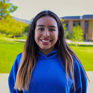 Natalie Ascorra has long brown hair and wears a blue sweatshirt outdoors.