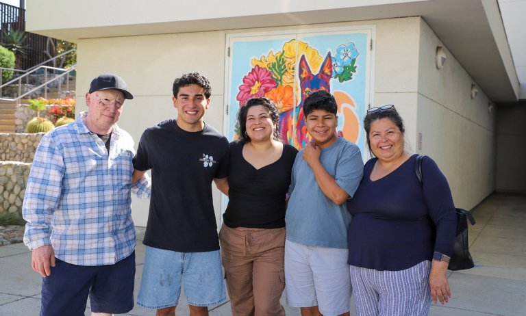 Sebastian and his family posing together in front of a mural