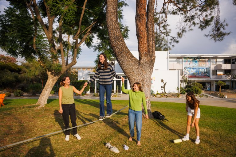 a girl walking across a slack line with friends on either side supporting her