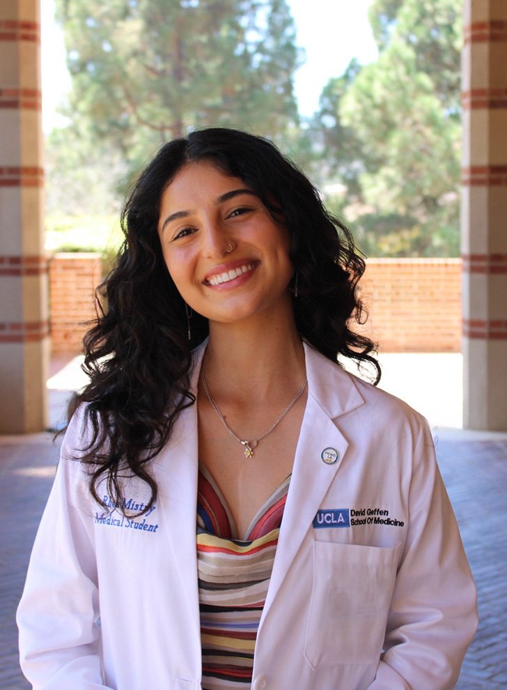 Rhea Mistry poses in an outdoor hallway in a white coat