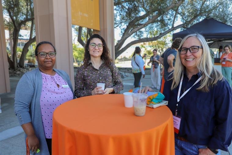three Pitzer deans stand around a round table with an orange tablecloth