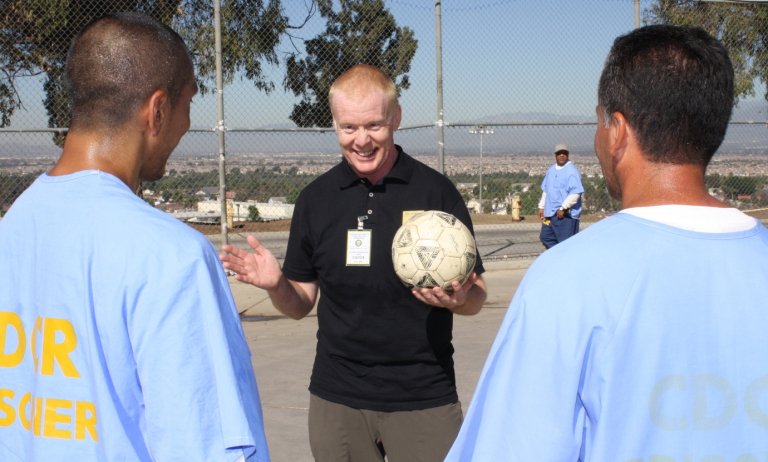 Nigel Boyle and two men from the CRC stand outside talking, while Nigel holds a soccer ball. 